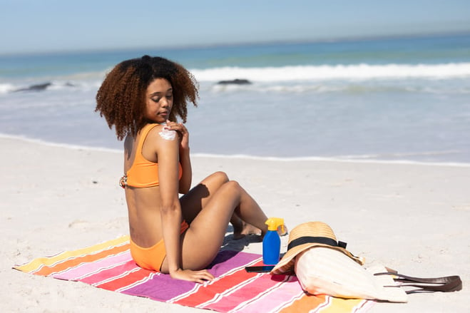 mujer afroamericana pasando por aplicar loción bronceadora a su piel