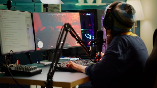 mujer jugando en la PC sobre su mesa gamer con dos monitores y un microfono de streaming
